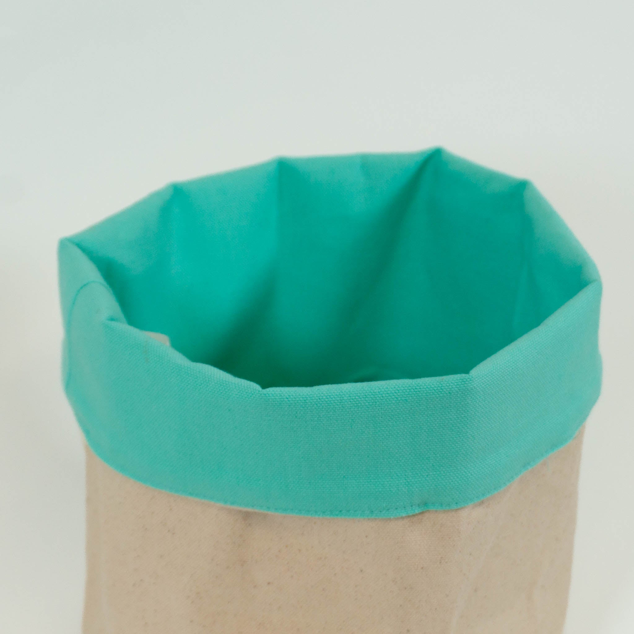 Close up of a cloth storage basket with the rim folded over to show the mint green inside color, with the beige color on the outside.
