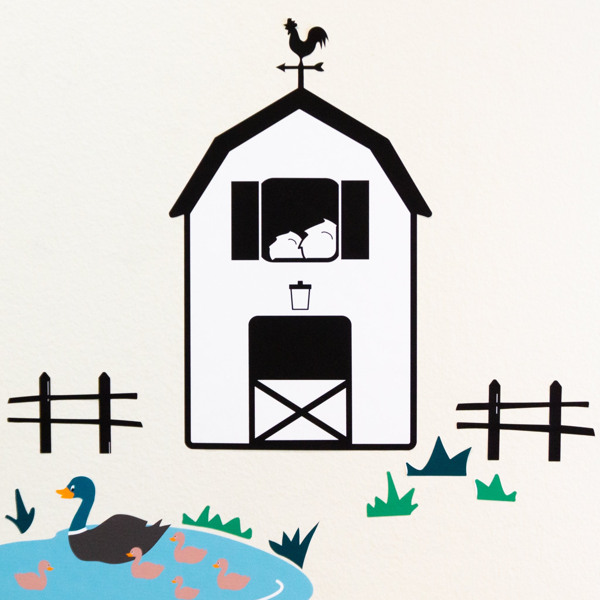 Black and white barn with rooster weathervane and fence next to green grass and ducks in a pond.