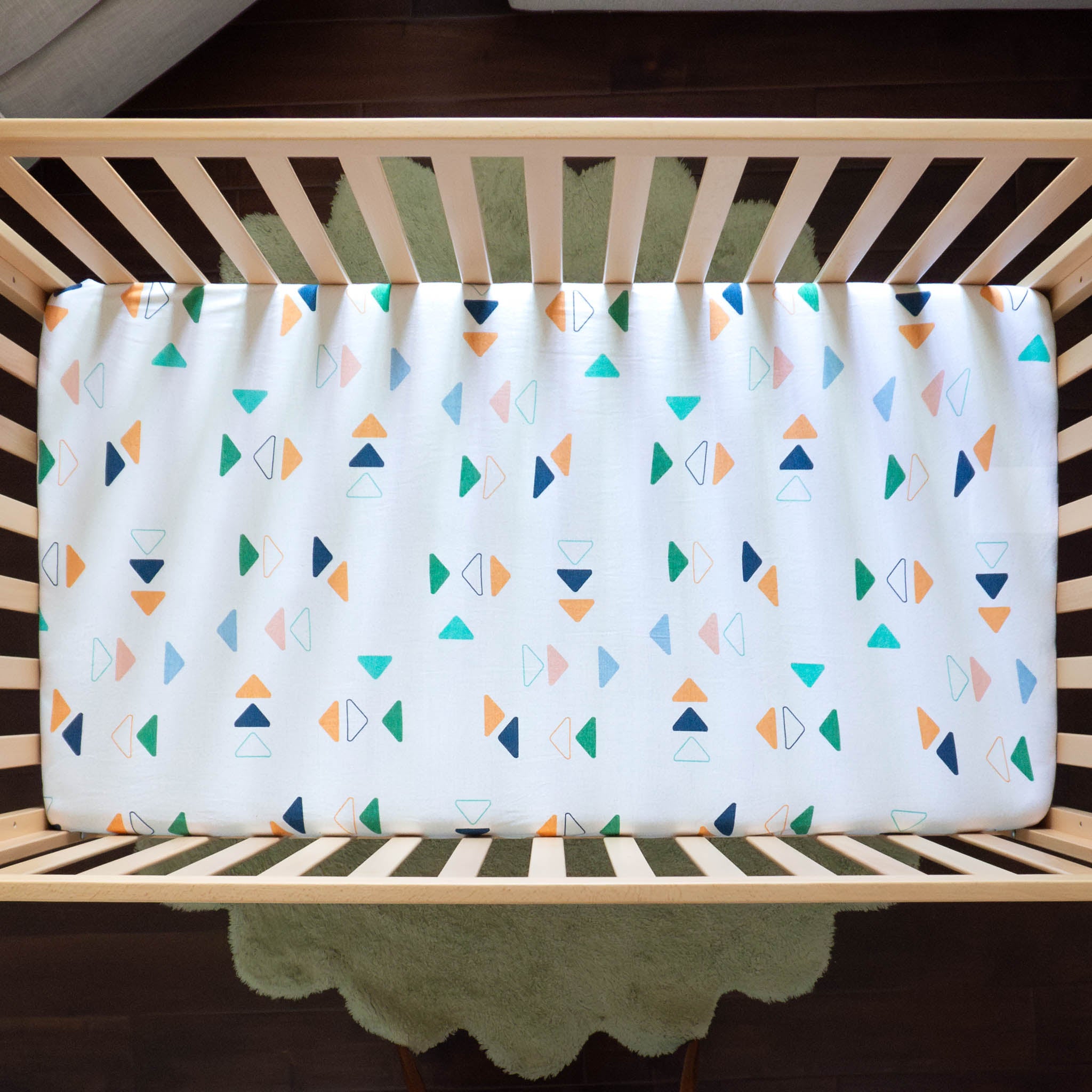 An aerial view of a white crib sheet with a repeated triangle pattern in different colors.