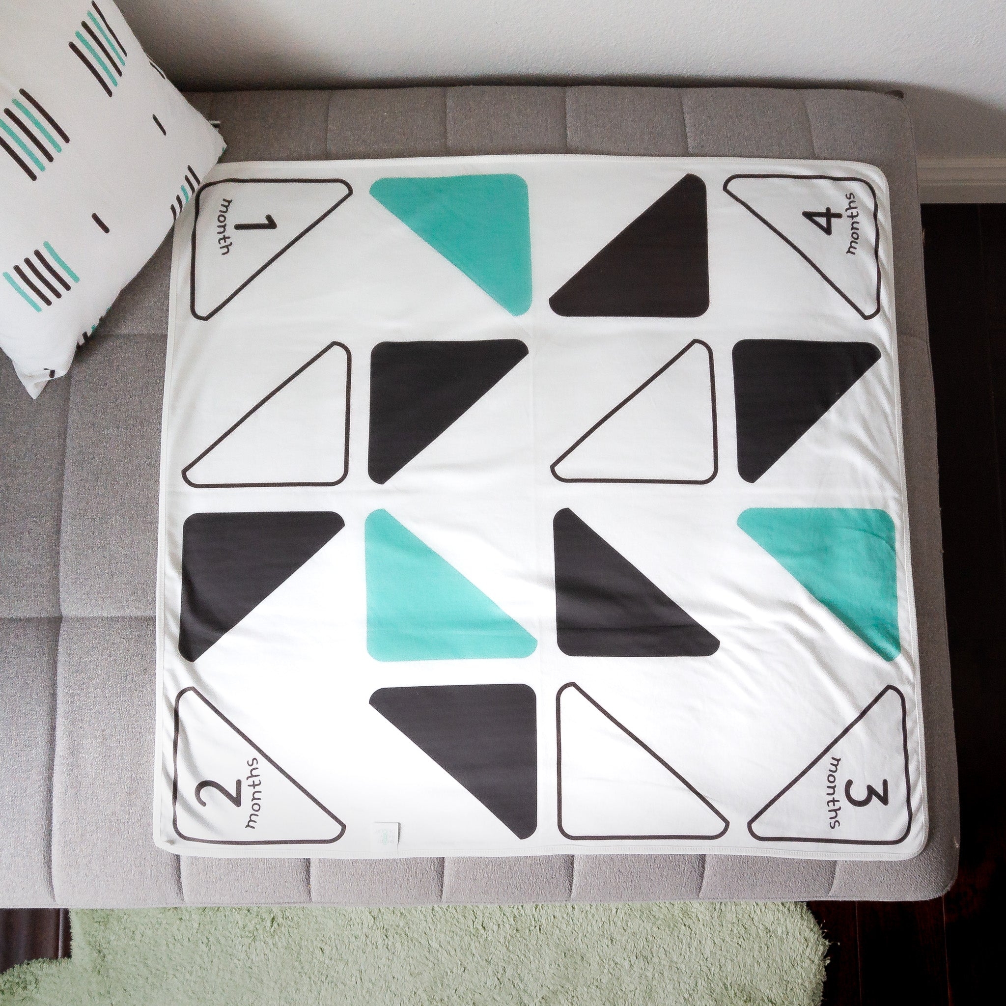 A baby blanket with black, mint green and white triangles displayed on a chaise sofa.