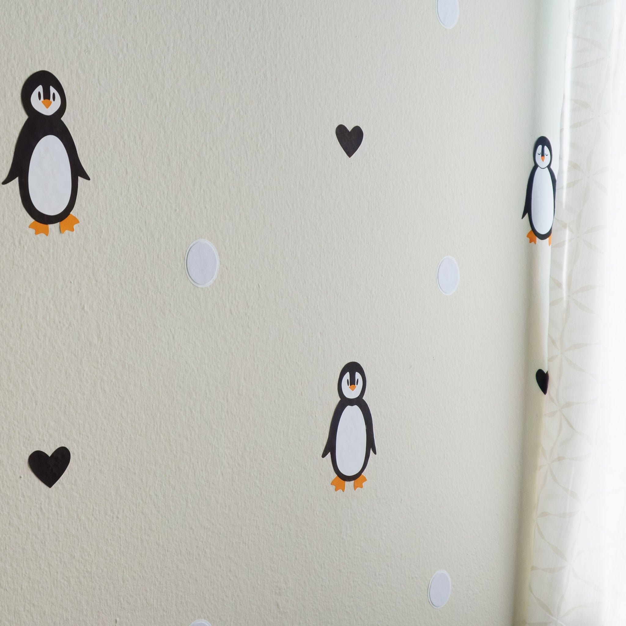 Alternating penguin and black heart wall decals on wall with curtain
