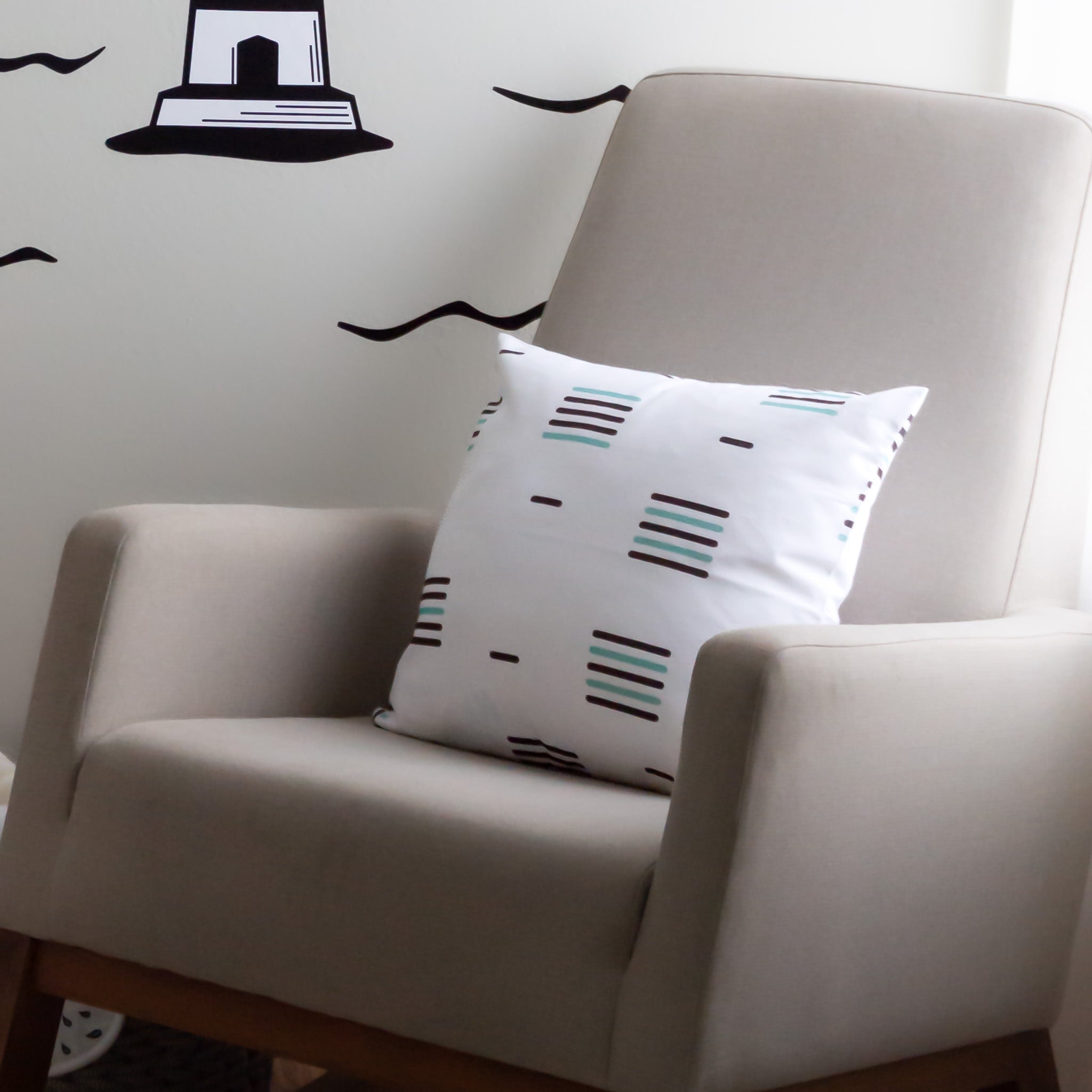 A throw pillow with a white background and black linear stripes, sitting on a rocking chair.