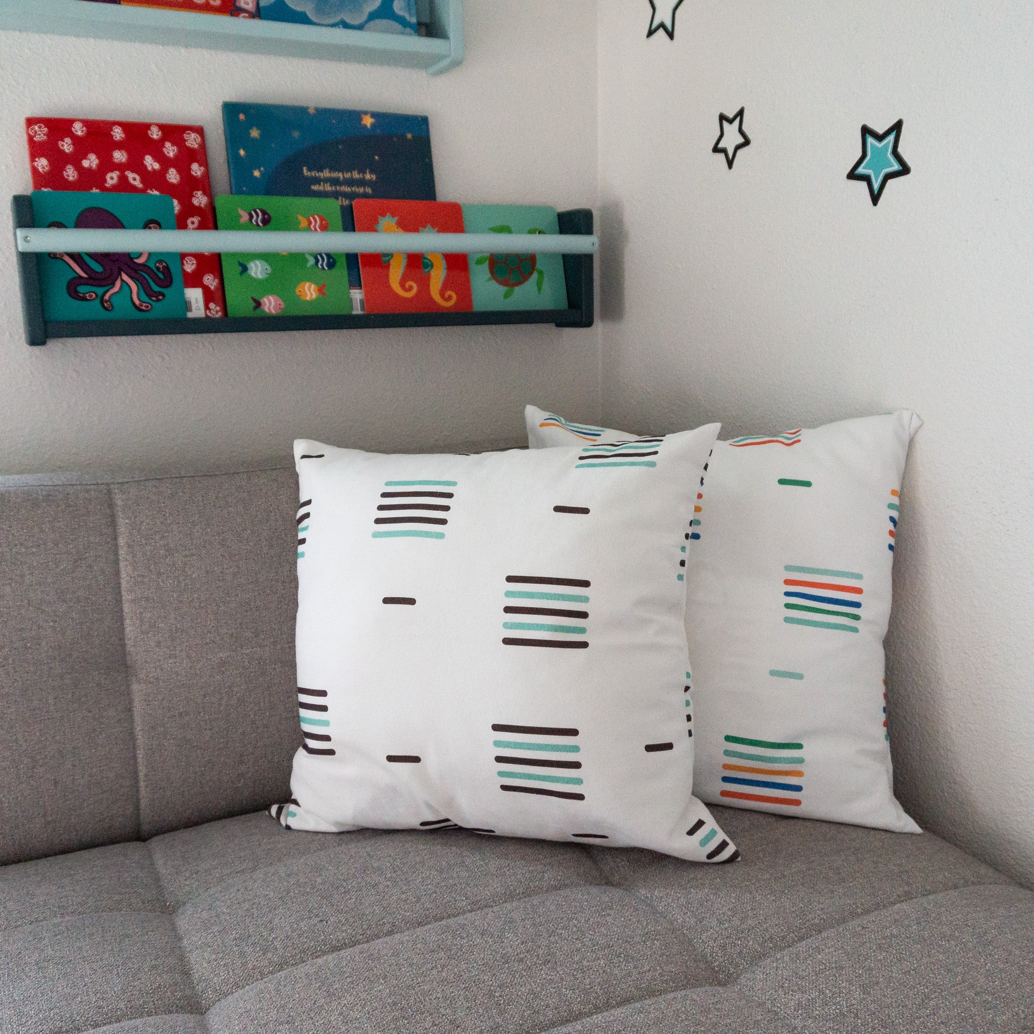 Two throw pillows sitting on a chaise sofa, both have similar linear patterns, one in black and white, the other is multicolored.