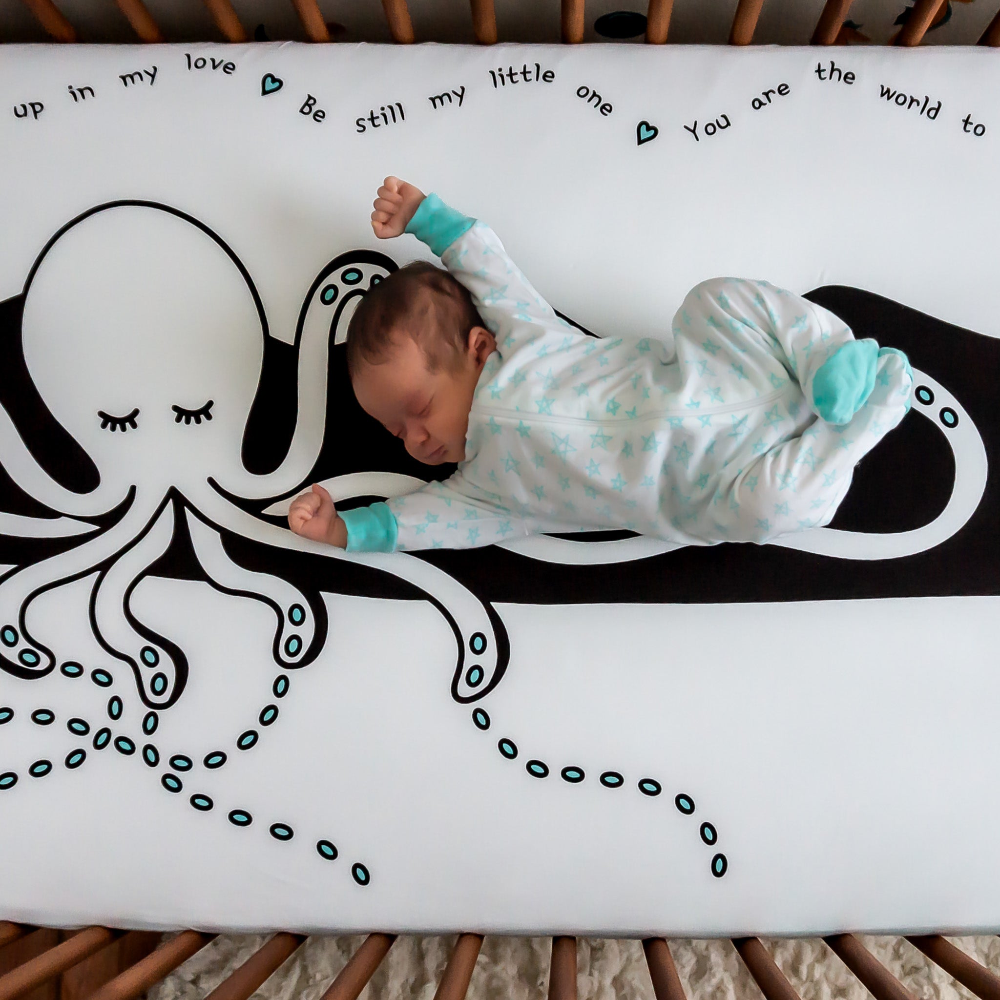 A baby lying on a black and white crib sheet with an octopus pattern on it, stretching his arms.