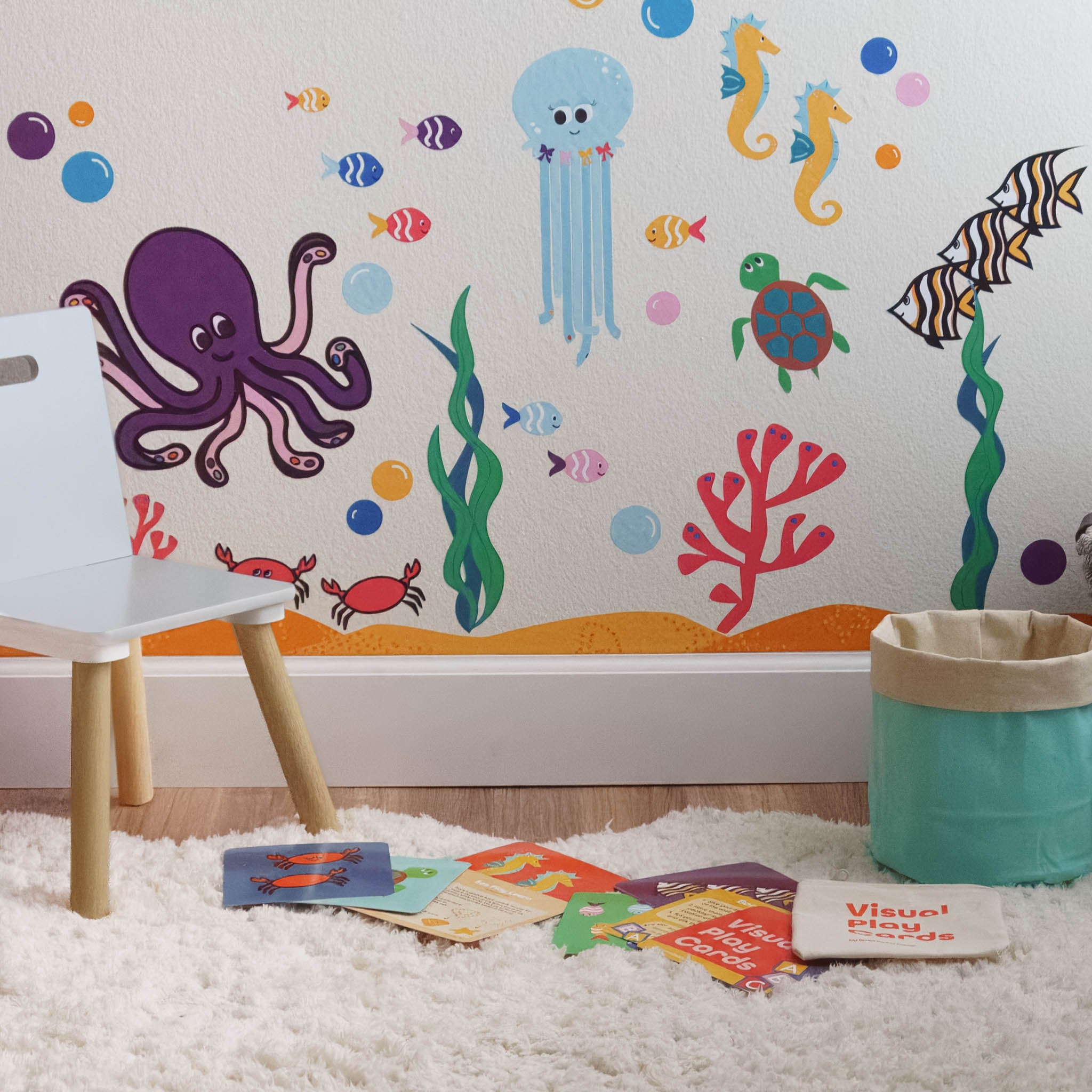 Wall with ocean wall art mural with cloth storage basket and visual play cards in front on the floor