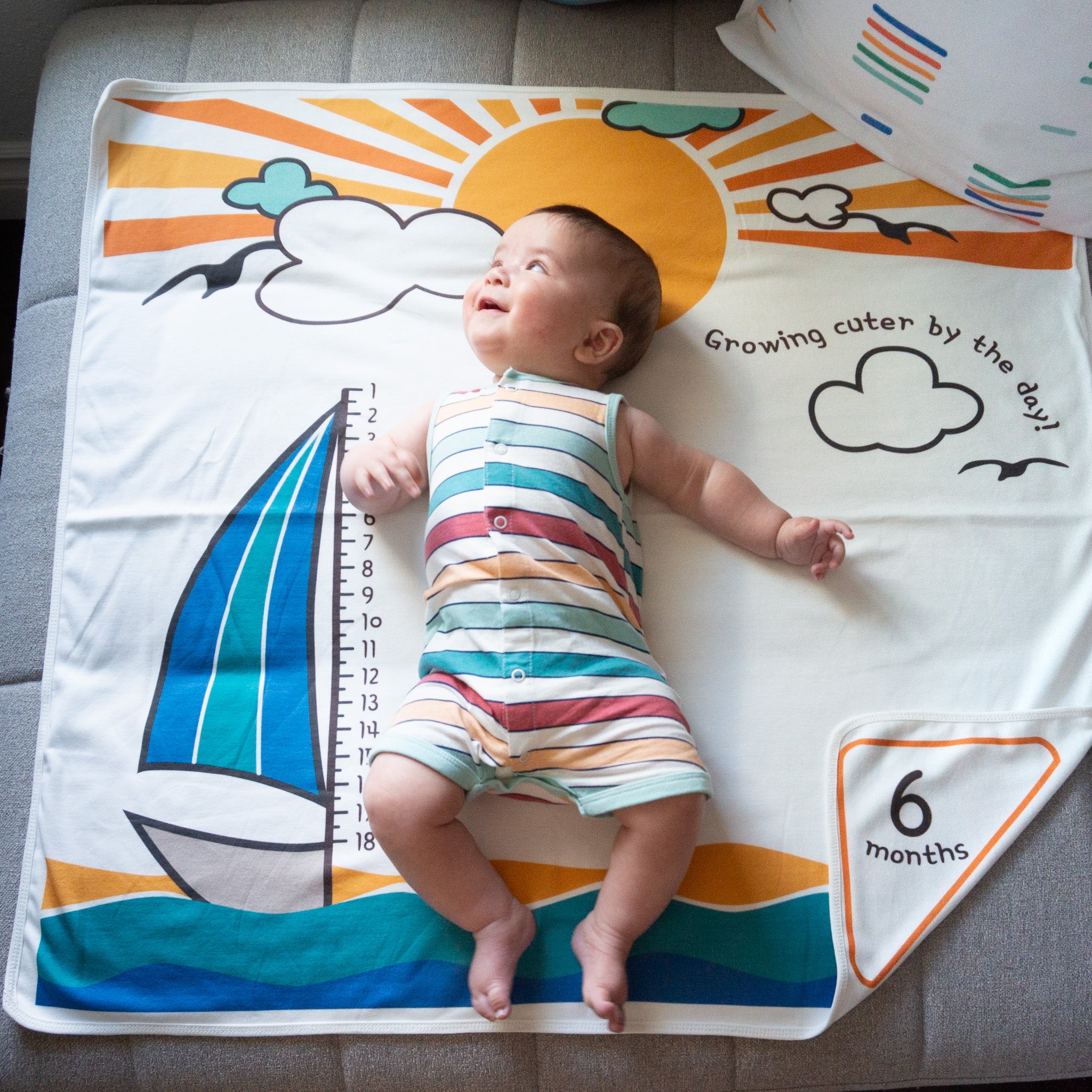 A baby lying on a blanket with a picture of a sailboat. The baby is smiling and looking up.