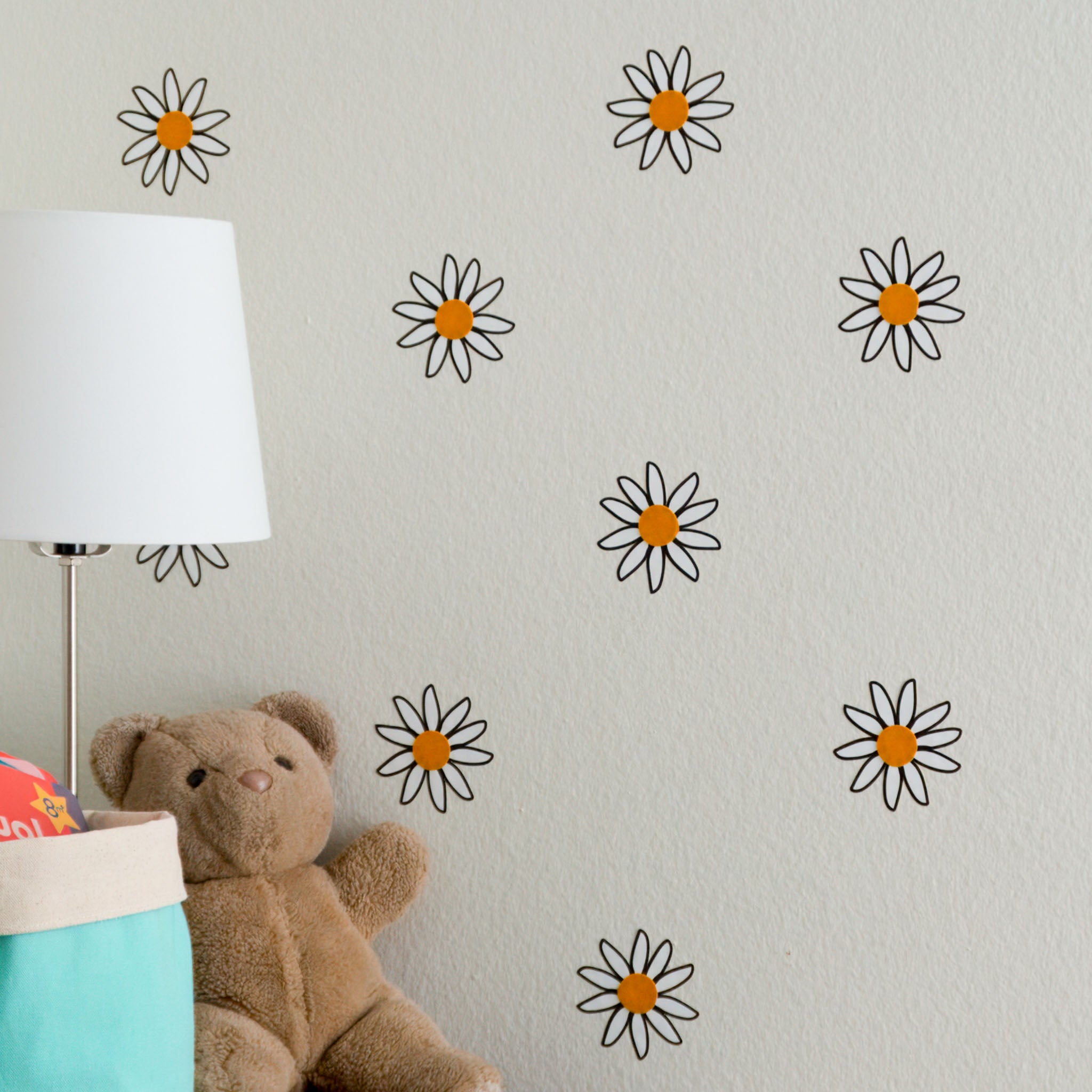 Wall of scattered daisy wall decals with teddy bear, storage basket and lamp in front